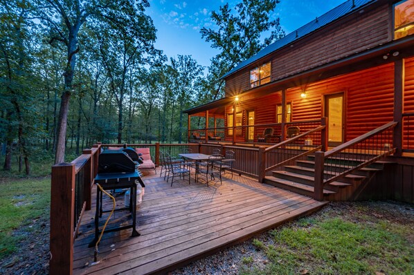 A wooden cabin with a deck, outdoor seating, and a grill.