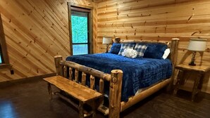 Ein Schlafzimmer einer Holzhütte mit Bett, Bank, zwei Nachttischen und einem Fenster.