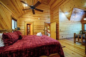 Interior de una cabaña de madera con una cama, un ventilador de techo y un comedor.