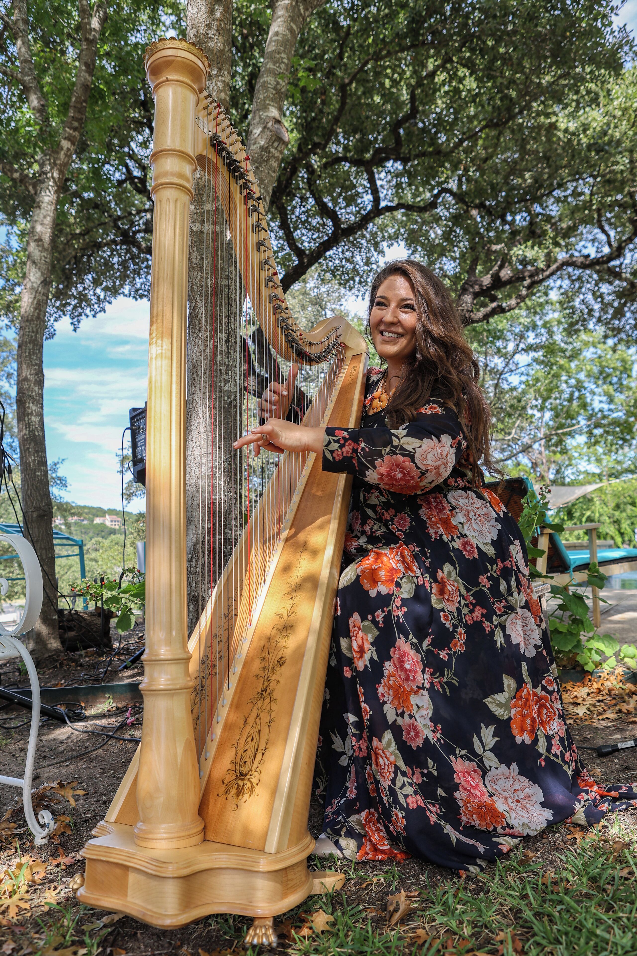 A harp with a wooden structure and strings, placed outdoors with trees in the background.