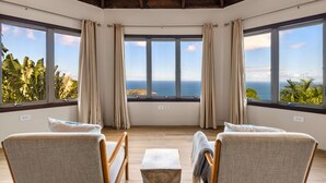 Habitació amb vista a l'oceà, dues cadires, una taula petita i una finestra amb cortines.