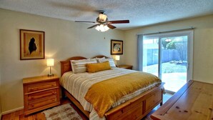 A bedroom with a bed, wooden nightstands, a ceiling fan, and a large window.