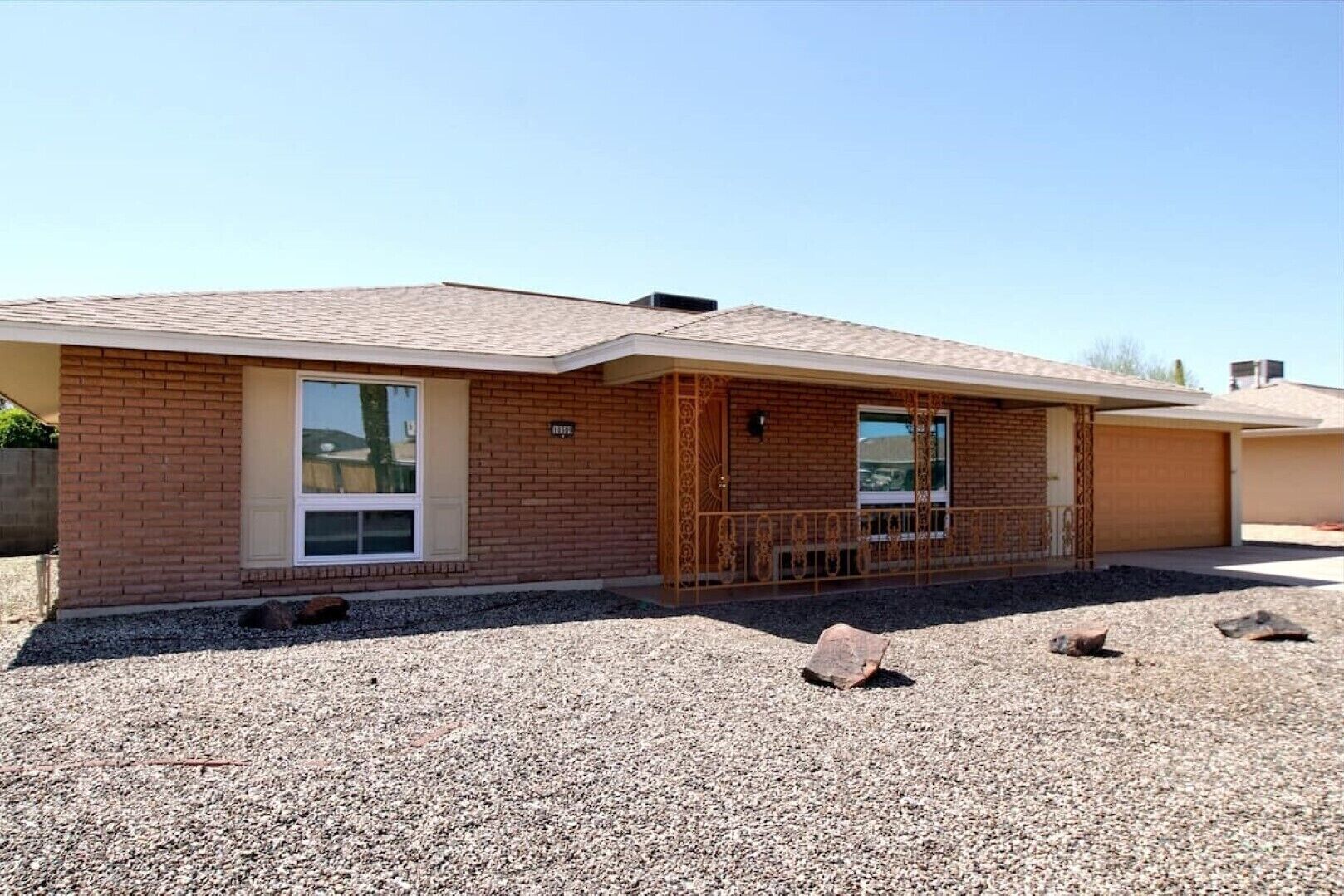 A single-story brick house with a front porch, a garage, and a gravel driveway.