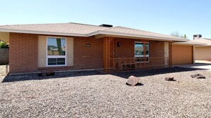 A single-story brick house with a front porch, a garage, and a gravel driveway.