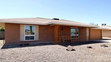 A single-story brick house with a front porch, a garage, and a gravel driveway.