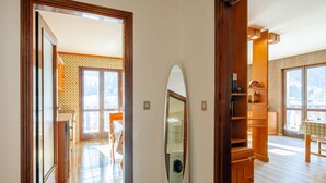 A hallway with a wooden floor, a large mirror, and a view into a room with a washing machine.