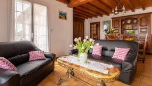 A living room with two black leather sofas, a wooden coffee table with a vase of flowers, and a wooden ceiling. - L'Albizia by Interhome (Gujan-Mestras)