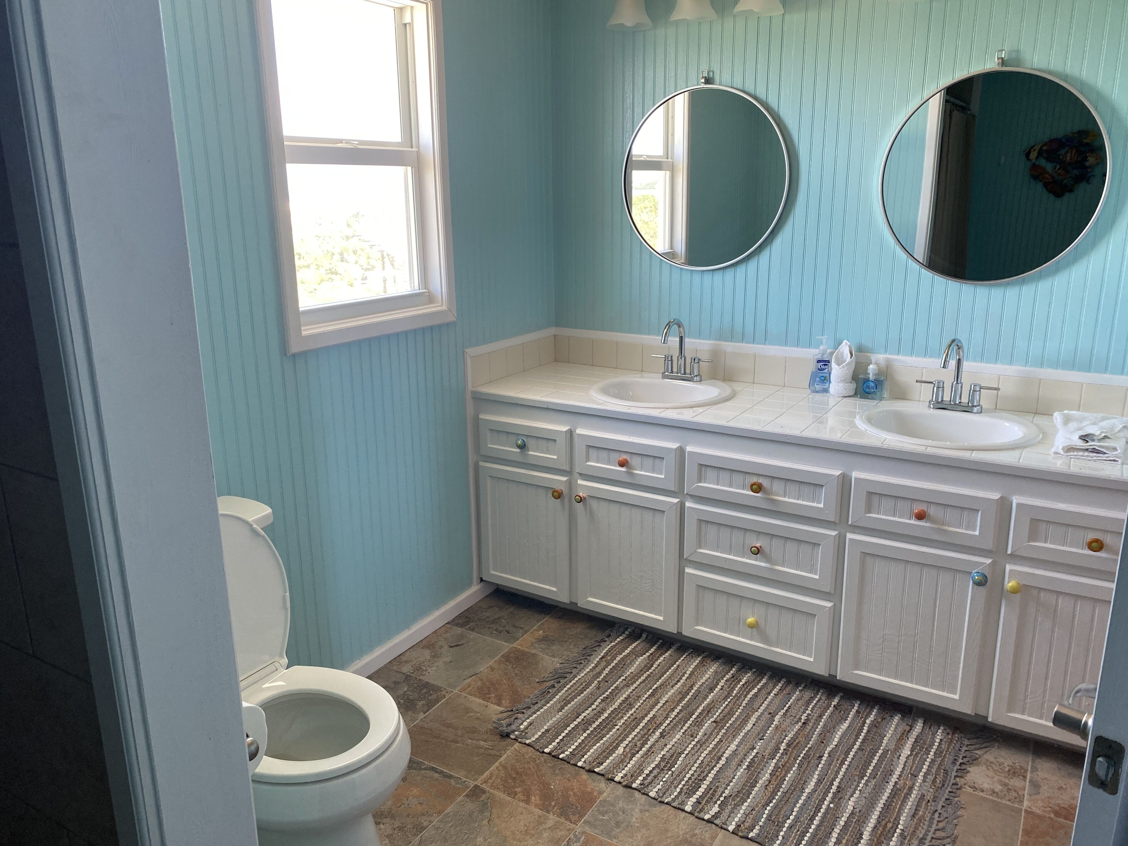 A bathroom with two sinks, a toilet, and a window.