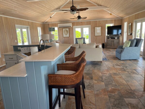 A spacious kitchen with a central island, bar stools, a dining area with a sofa, and a television.