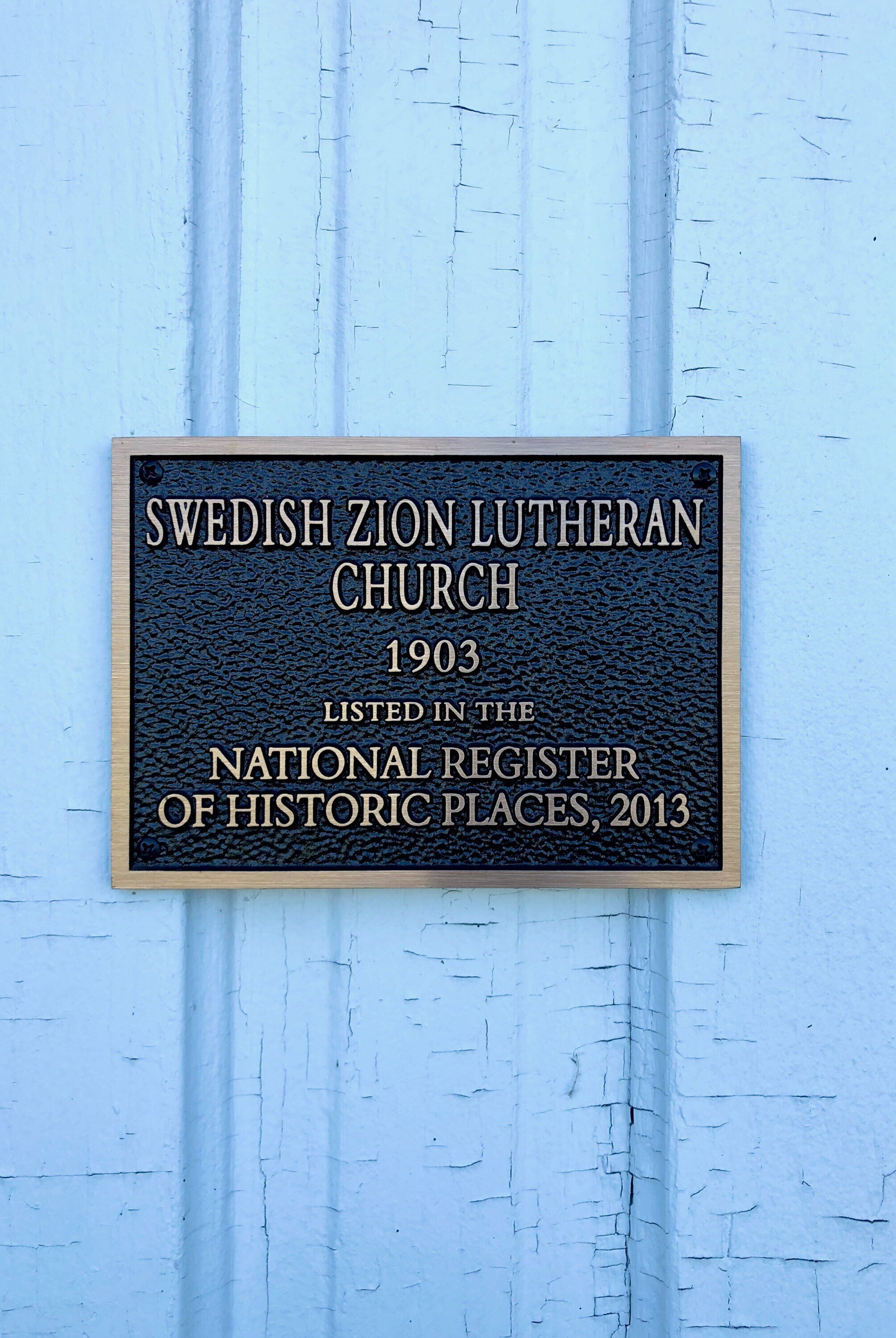 Una placa en una pared con el texto 'Iglesia Luterana Sueca Zion 1903 Incluida en el Registro Nacional de Lugares Históricos, 2013'.