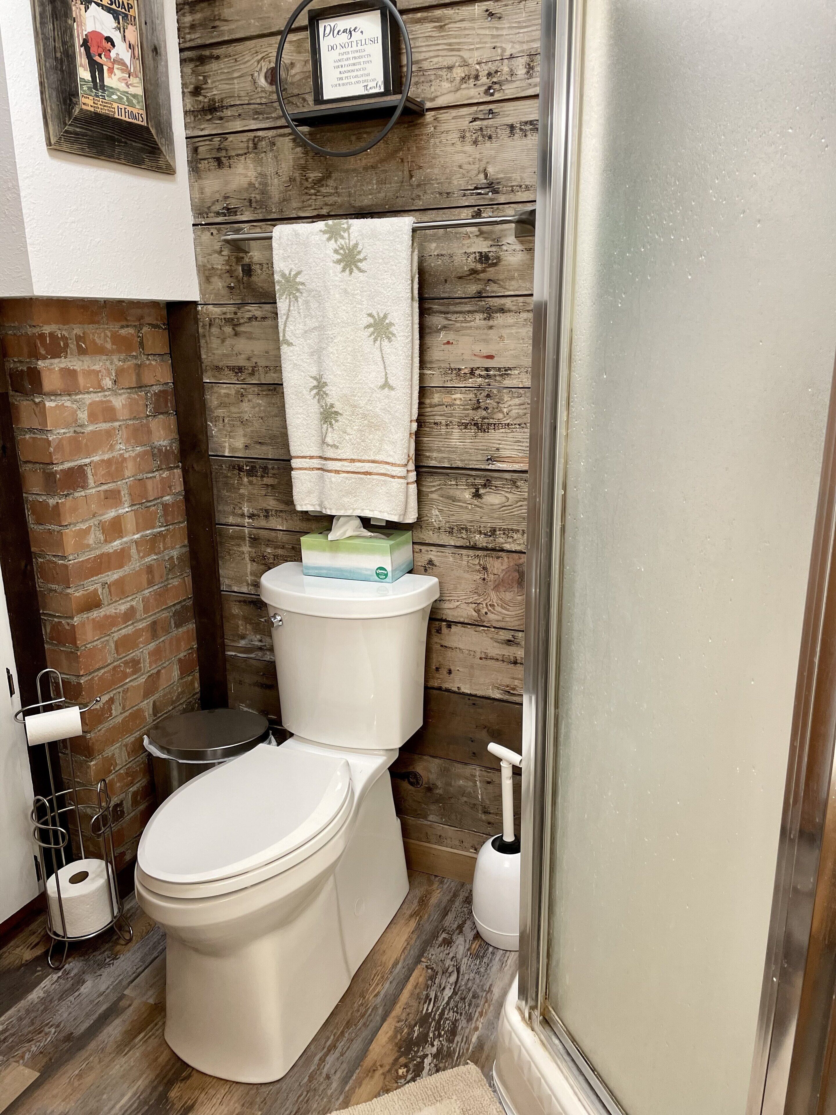 Een badkamer met een houten wand, toilet, handdoekrek met handdoek en een zakdoos.