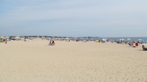 Ein weiter Sandstrand mit mehreren Sonnenschirmen und Liegestühlen, einem Rettungsturm und freiem Blick auf den Ozean.