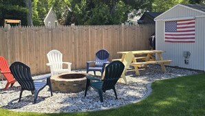 Ein Garten mit einer Holzterrasse, einer Feuerstelle und Sitzmöbeln.