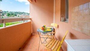 A balcony with a table set for two, a chair, and a view of the cityscape. - Nice apartment for 2 people with WIFI, A/C, TV, balcony and pets allowed (Cavalaire-sur-mer)