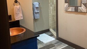 Une salle de bain avec un lavabo en cuivre, un miroir avec un cadre en bois et un espace douche avec un mur carrelé.