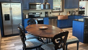 Une cuisine moderne avec des meubles bleus, des appareils en acier inoxydable et une table à manger en bois, assortie de chaises rembourrées.