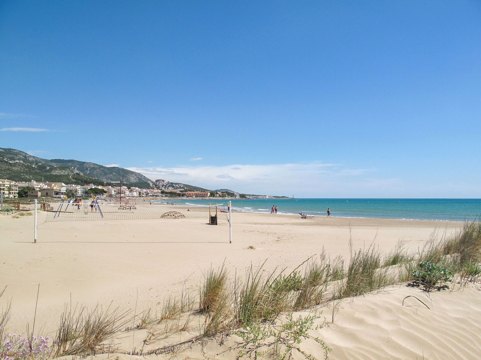 A beach with a volleyball net, sand dunes, and a clear blue sky.