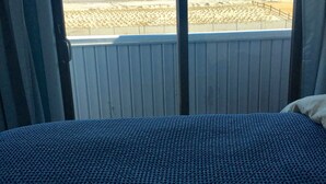 Habitació amb un llit i vista a una platja a través d'una finestra gran.