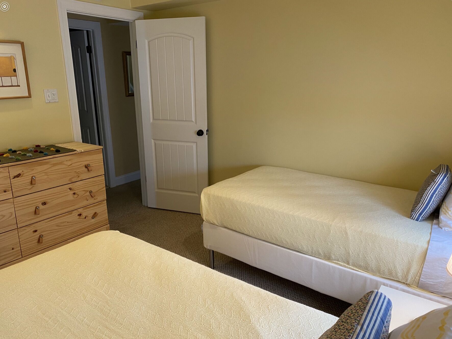 Un dormitorio con un aparador de madera, una cama con almohadas y una puerta que da a otra habitación.
