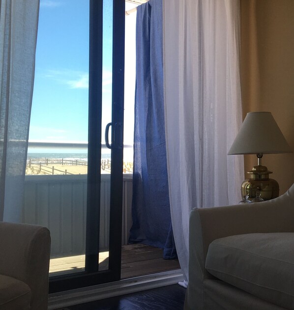 A room with a view of the beach, a sliding glass door, a lamp, and a chair.