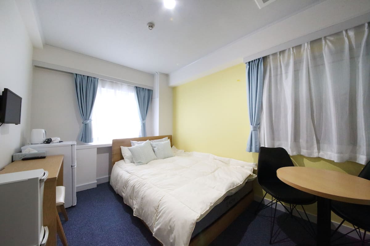 A hotel room with a bed, a desk with a chair, a small table, and a television.