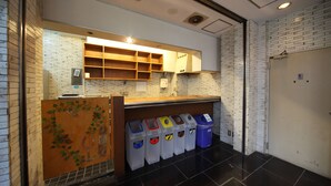 A clean, modern bathroom with a tiled floor, a sink, and a toilet. There are trash bins and a wooden panel with a vine design.