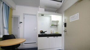 A compact kitchen with a sink, stove, and cabinets, a small dining table with chairs, and a door with a sign.