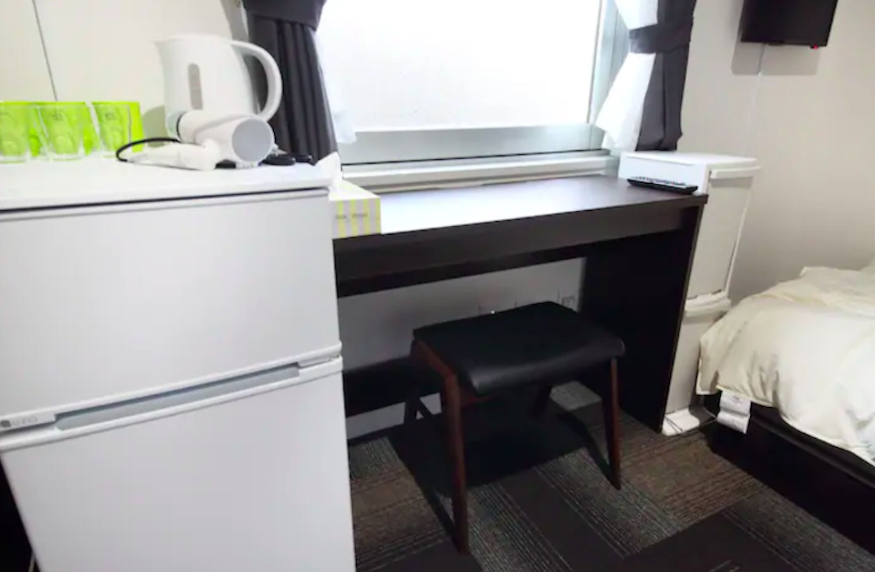 A compact hotel room with a kitchenette, a small desk, a chair, and a bed.