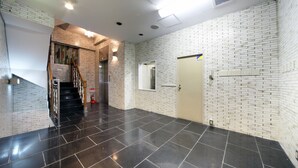 A spacious lobby with a black tiled floor, white brick walls, and a wooden staircase.