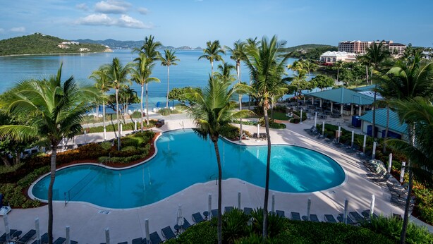 Piscina do resort com espreguiçadeiras, palmeiras e vista para o mar.