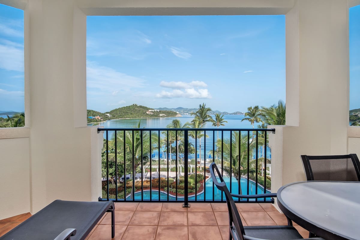 A balcony with a view of a pool and surrounding landscape.