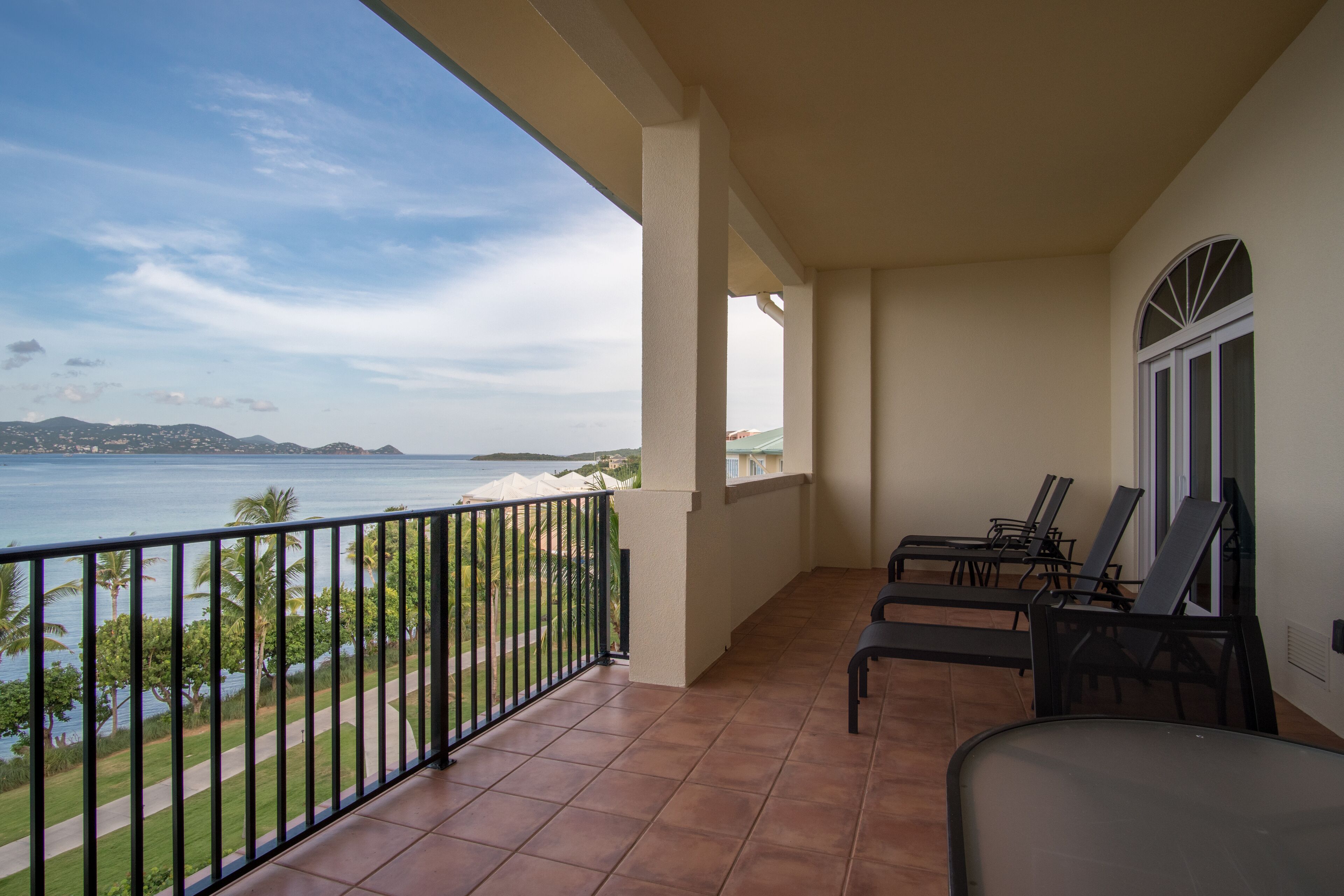 A balcony with a view of the sea, equipped with black lounge chairs and a tiled floor.