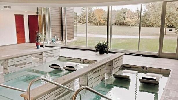 A modern indoor swimming pool with clear glass walls, a tiled floor, and a view of a grassy area outside. - Charming guest house on 1.5 acre lake front property (Green Lake)