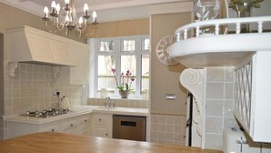 A kitchen with a wooden countertop, white cabinets, a built-in oven, and a window with flowers. - Large four bedroom home near country walks & beach (Shanklin)