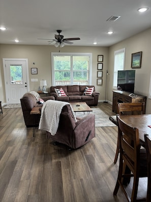 A living room with a brown sofa, a coffee table, a TV stand, and a dining table with chairs.