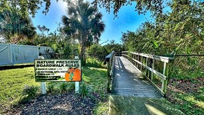 Une promenade surélevée en bois, aménagée dans une réserve naturelle, avec un panneau indiquant les règles et un pont en bois.