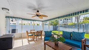 Un patio couvert avec un ventilateur de plafond, une table à manger avec des chaises, un canapé agrémenté de coussins à motifs et une plante en pot.