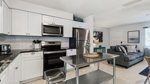Une cuisine moderne avec des meubles blancs, des appareils en acier inoxydable et un coin repas doté d’une table grise.