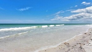 Une plage avec une eau d’un bleu limpide et un rivage sablonneux.