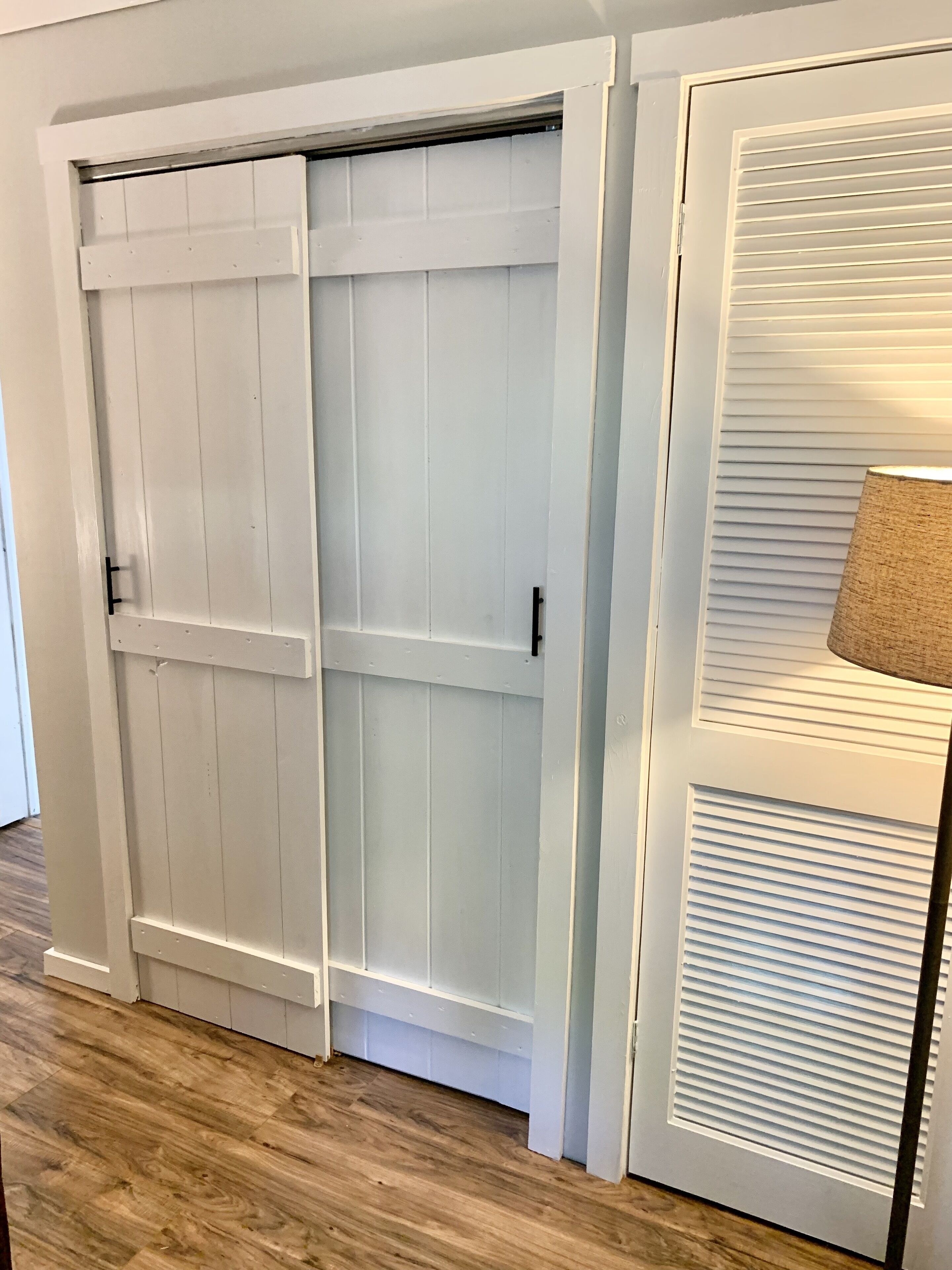 A white sliding door with a black handle, a white door with horizontal blinds, and a wooden floor.
