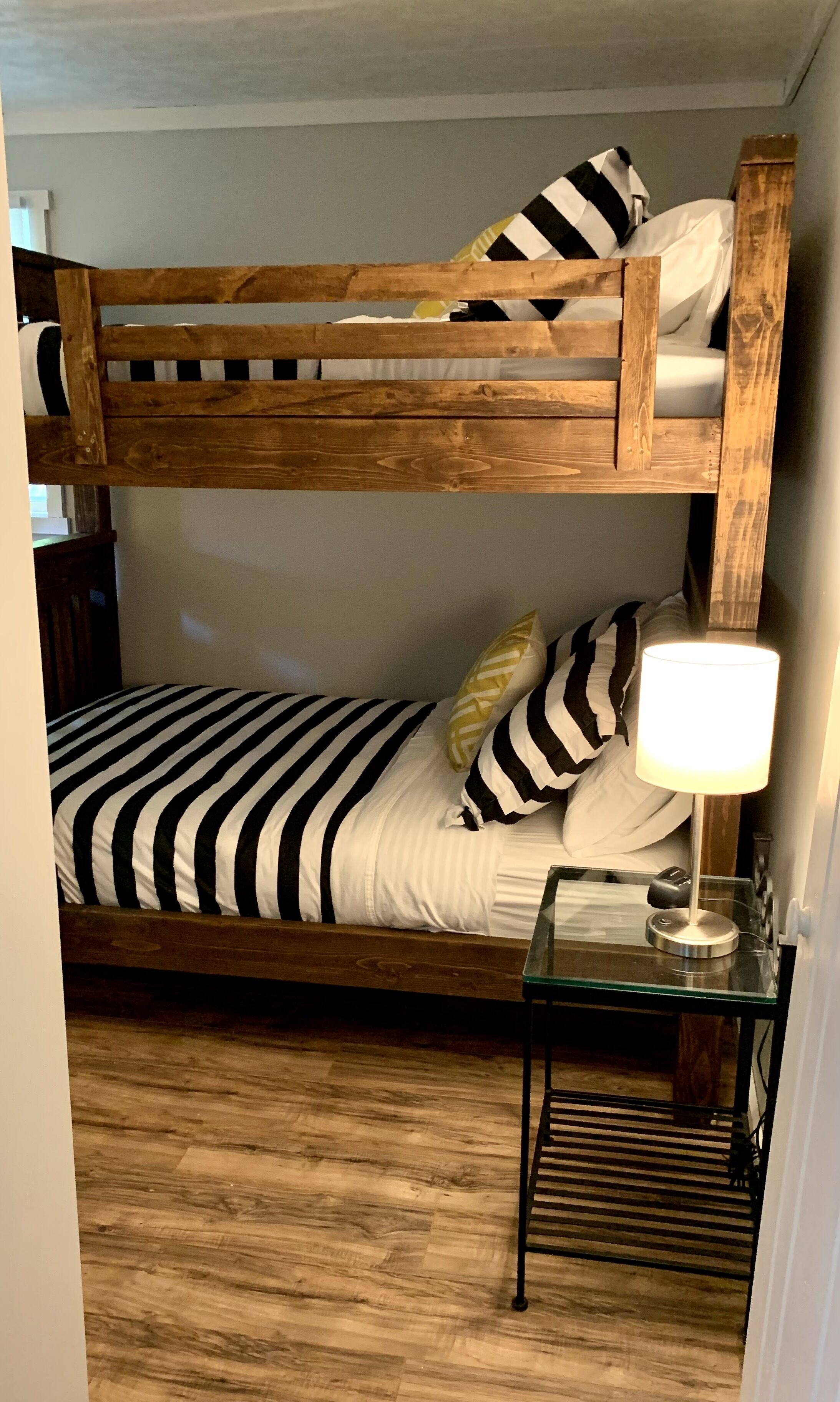 Una cama litera con ropa de cama a rayas, una lámpara de noche y una mesita con un teléfono.
