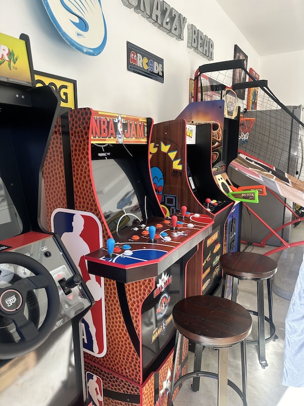 Uma sala de jogos retrô com NBA JAM e outros jogos, com controles joystick e um aro de basquete.