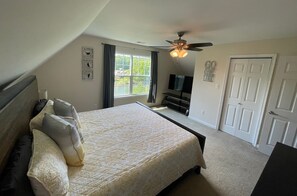 Ein Schlafzimmer mit Bett, Deckenventilator, Fernseher und einer Tür.