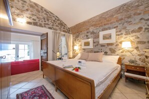 Ein Schlafzimmer mit Steinsandsteinwand, einem hölzernen Bett, einem Nachttisch, einem roten Sofa und Blick ins Freie.