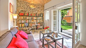 A cozy living room with a stone wall, a bookshelf, a sofa with red cushions, and a glass coffee table. - Casa Tamè - Pieds dans l'eau, Melide, Switzerland (Melide)