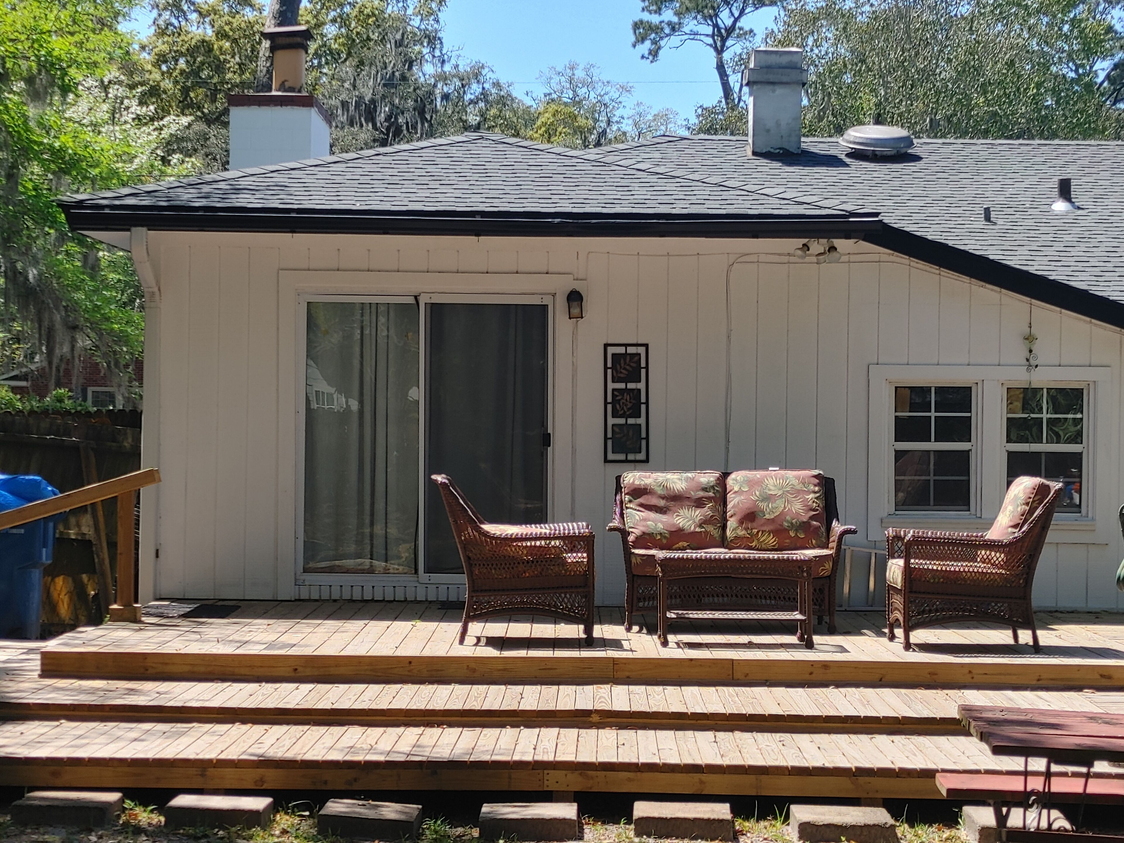 A white building with a porch, two wicker chairs, a bench, and a small table.