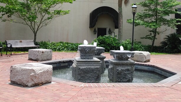 Ein Innenhof mit einem Brunnen, Bänken und einem Gebäude mit großem Bogenportal.