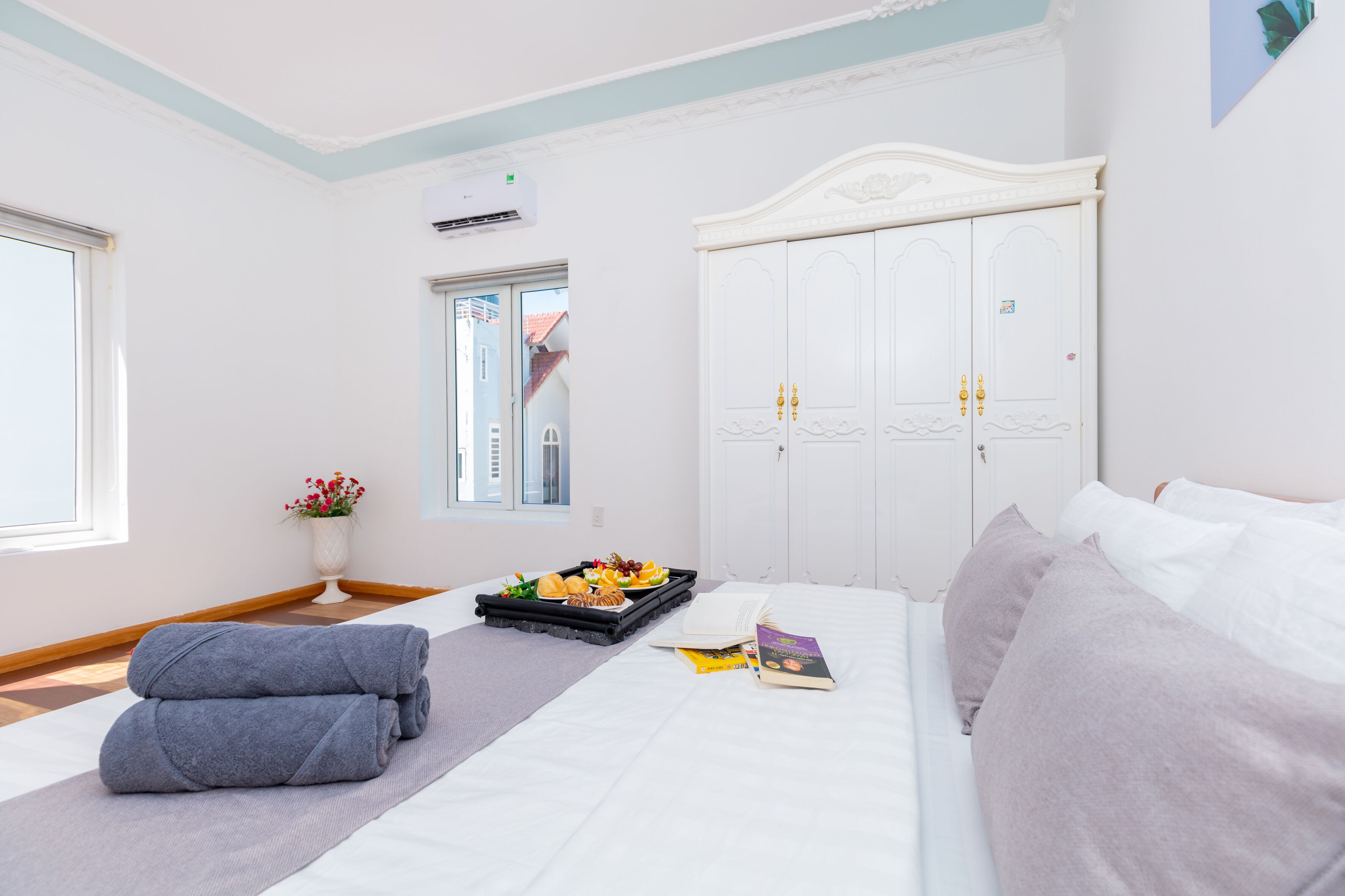 Quarto de hotel com uma cama, mesa de cabeceira com bandeja de comida, um livro e janela com vista para o exterior.