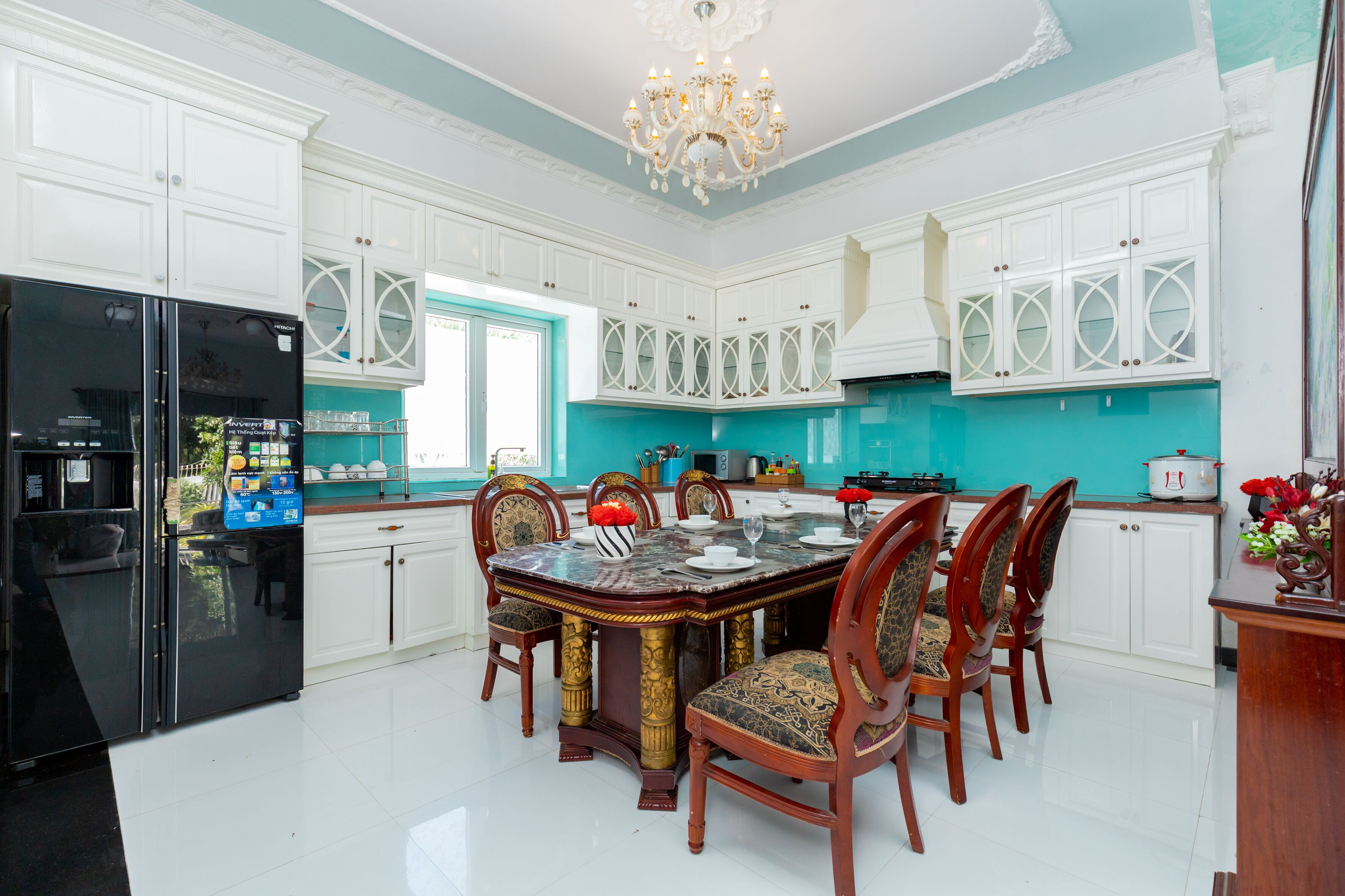 A spacious kitchen with white cabinets, a black refrigerator, and a dining table set for six.