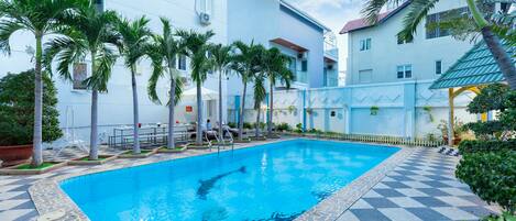A swimming pool surrounded by palm trees and a building with a checkered floor pattern.